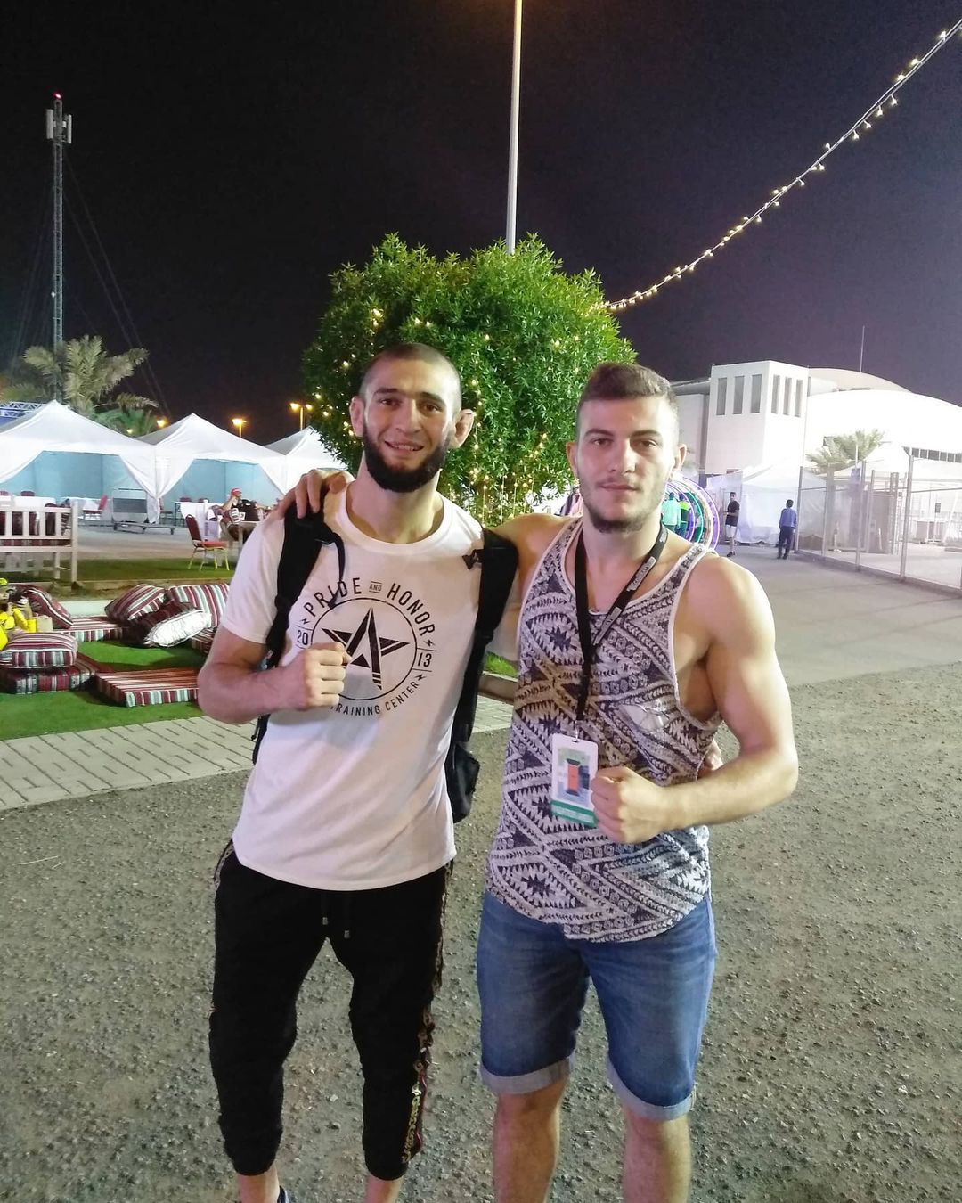 Marco con il braccio sulla spalla di Khamzat Chimaev, di notte vicino alle tende bianche di un evento a Bahrein