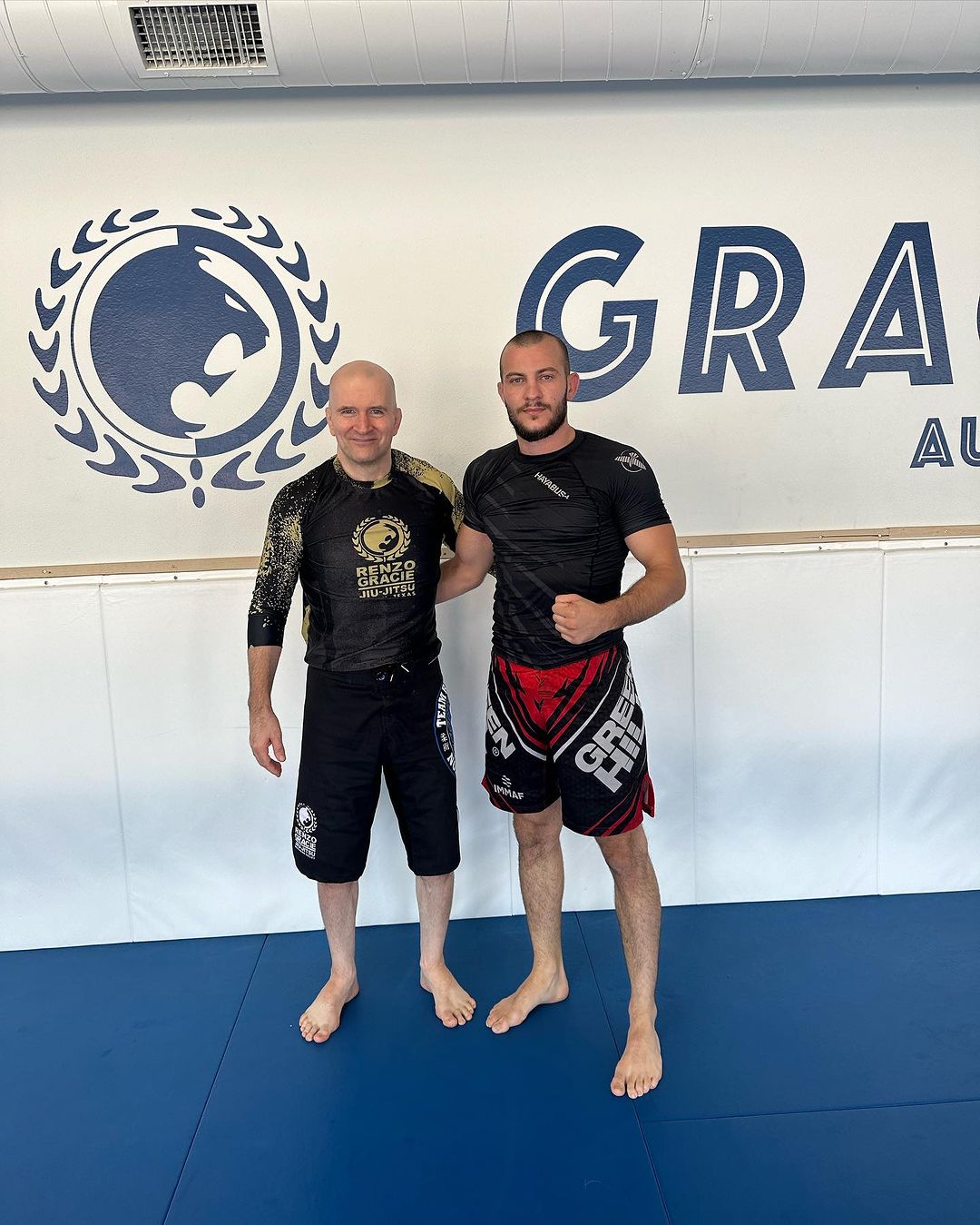 Marco insieme a John Danaher in piedi sul tatami blu della palestra Renzo Gracie Austin, entrambi in rashguard