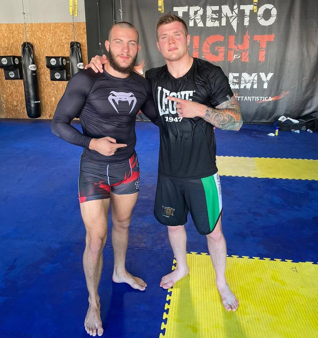 Marco Doda e Marvin Vettori in posa sul tatami blu di una palestra, davanti a un striscione della palestra di Trento