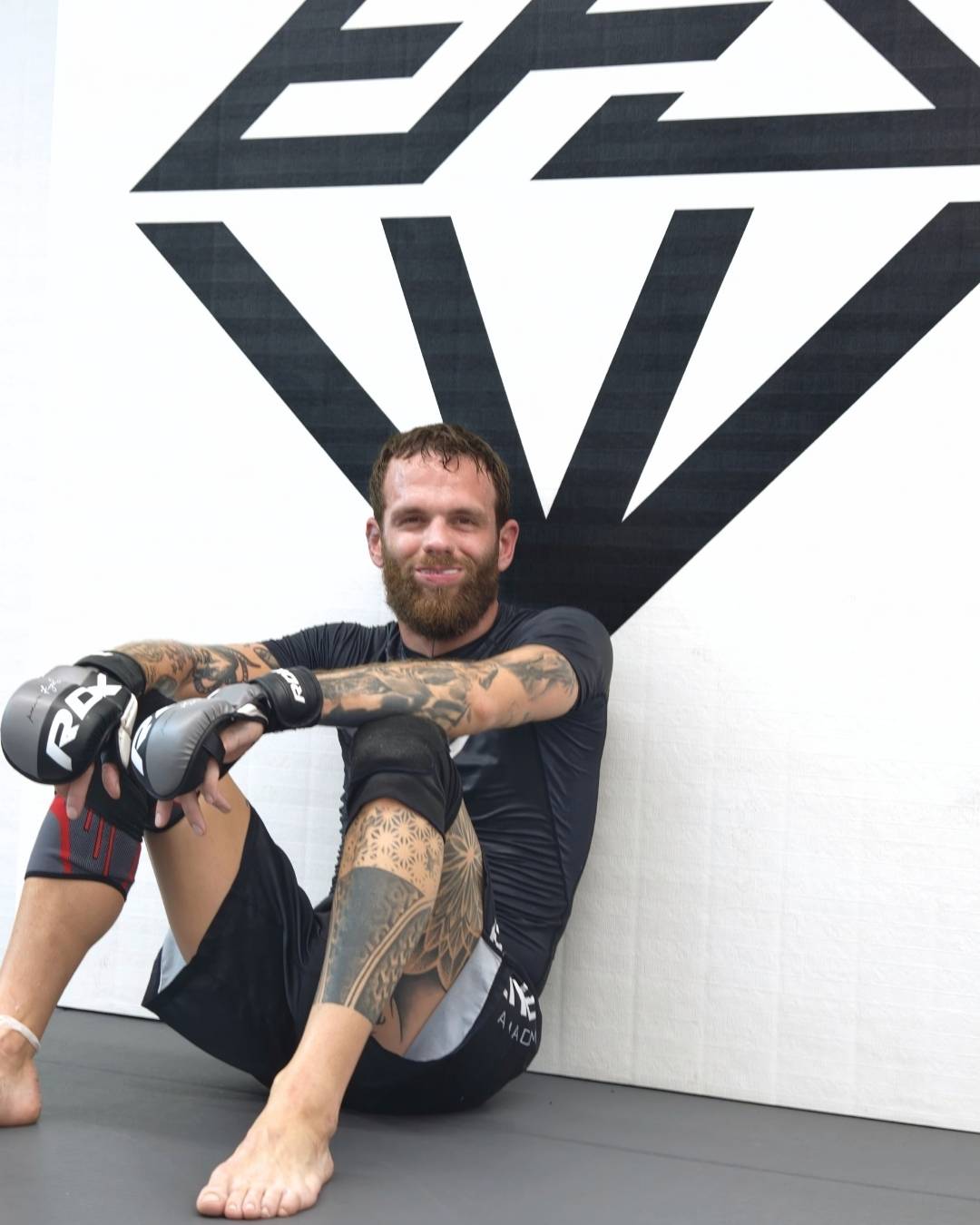Atleta di MMA seduto a terra sul tatami, con guantini e ginocchiera
